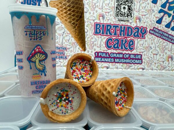 A stylish and colorful box labeled 'Trippy Tips Birthday Cake Blue Meanies Shrooms Cone Master Box,' showcasing pre-rolled cones filled with a blend of Blue Meanies mushrooms and birthday cake flavor. The cones and packaging highlight the product’s convenience, quality, and unique flavor combination